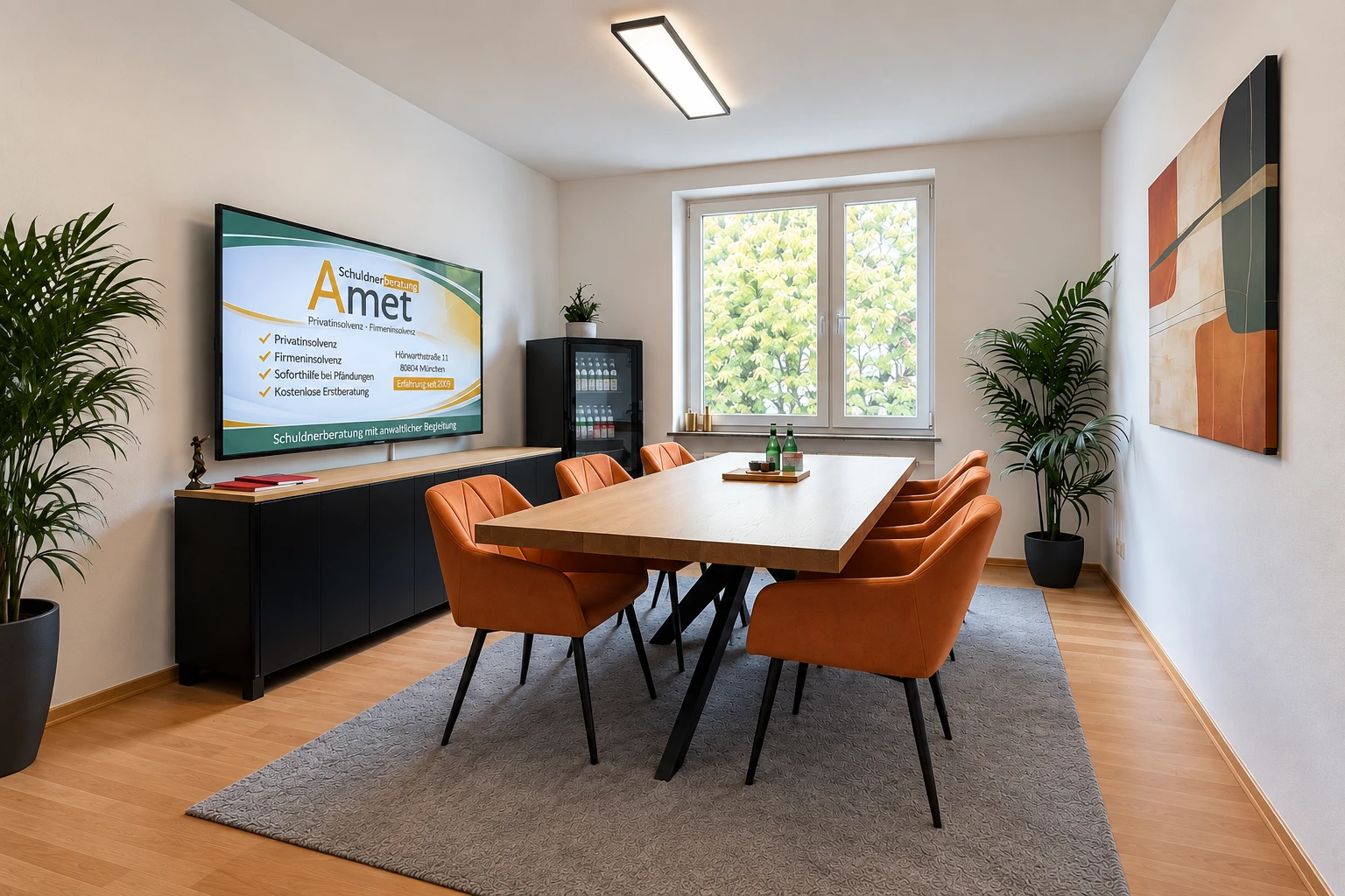 Besprechungsraum der Schuldnerberatung Amet in München/Schwabing mit Besprechungstisch, orangefarbenen Stühlen und Bildschirm mit dem Amet-Logo