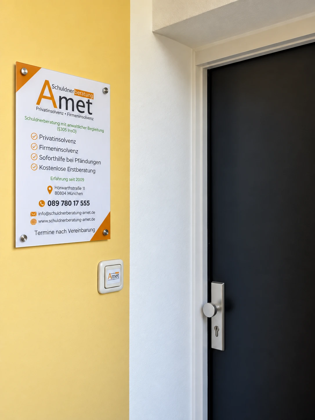 Türschild der Schuldnerberatung Amet neben dem Eingang: Leistungen, Adresse Hörwarthstraße 11 und Telefonnummer
